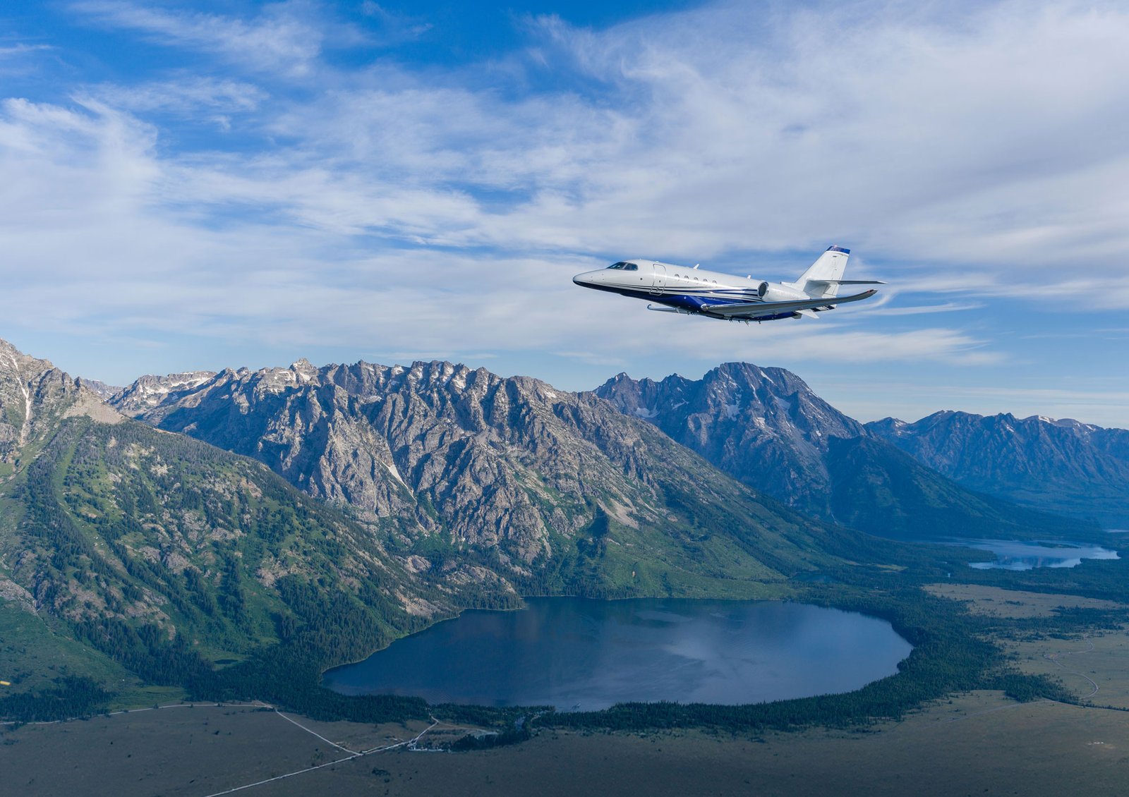 Super-midsize jet cruising above a snow-capped mountain range with a lake below