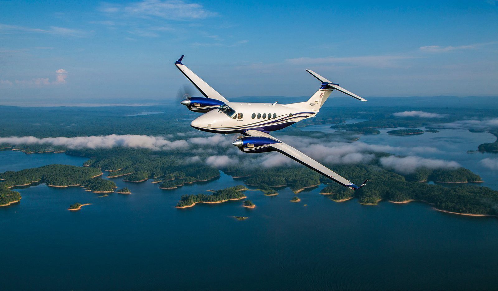 Twin engine King Air turboprop above a cloud layer with forested lakes below