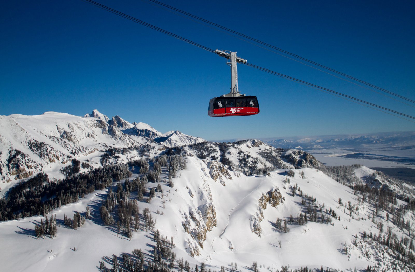Red aerial tram car climbing above a snow covered ridge with the valley below