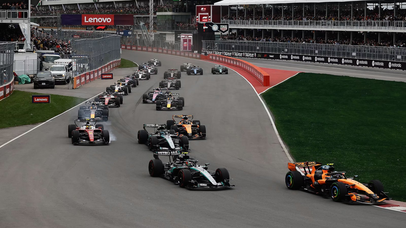 Formula 1 field racing wheel to wheel out of a corner past the grandstands
